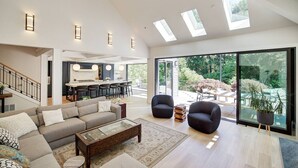 A spacious living area with a large sofa, two armchairs, a coffee table, and a dining area with a kitchen in the background. - Luxury Wooded Estate With Pool (Sammamish)
