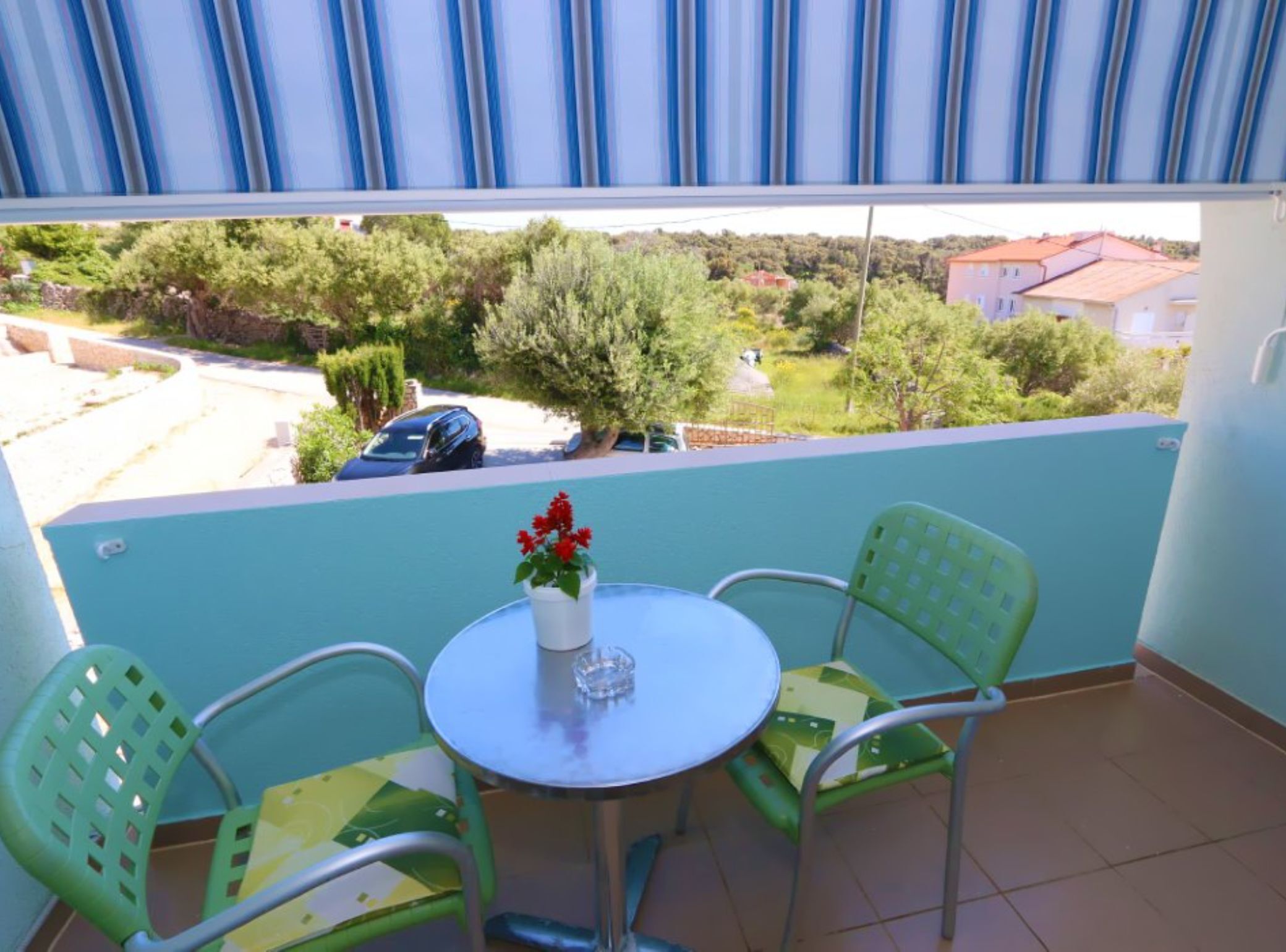 Un balcón con una mesa redonda y dos sillas, una planta en maceta y vistas a una zona residencial.