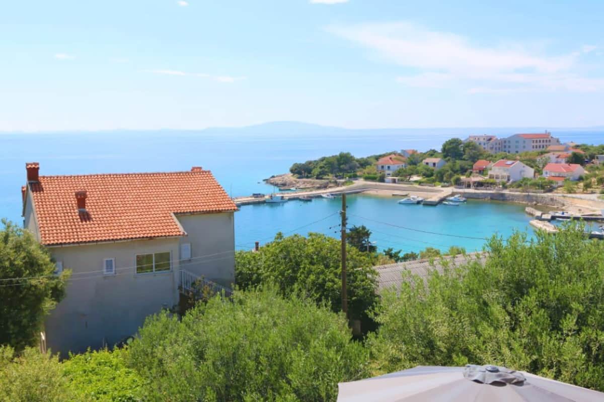 A coastal view with a house, a marina, and buildings in the background.