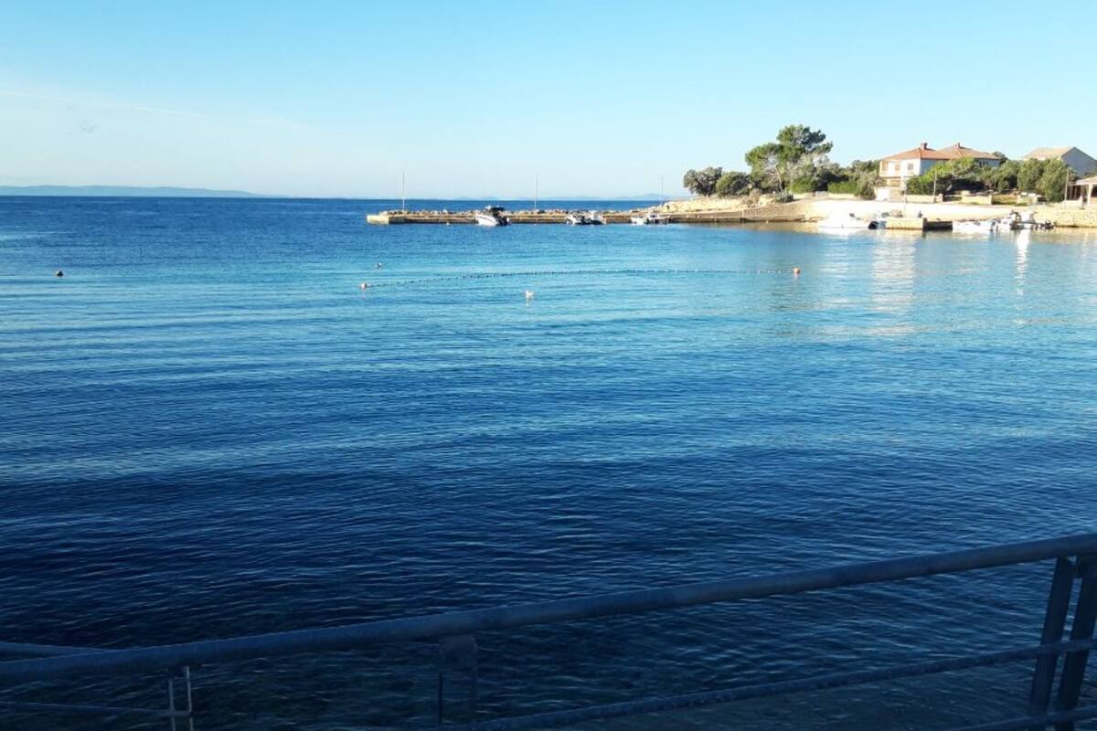 A coastal view with calm waters, a pier, and buildings in the background.