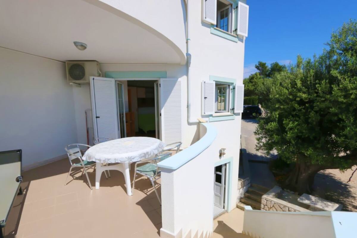 A balcony with a table and chairs, a sliding door, and a view of a tree and a parked car.