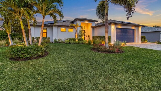A modern two-story house with a well-maintained lawn, palm trees, and a garage. - Waterfront Dream! Saltwater Pool, Sauna, & Boat dock 4 bed 3 bath on the water (Cape Coral)