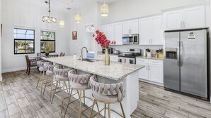 A modern kitchen with white cabinets, stainless steel appliances, and a central island with bar stools. - Waterfront Dream! Saltwater Pool, Sauna, & Boat dock 4 bed 3 bath on the water (Cape Coral)