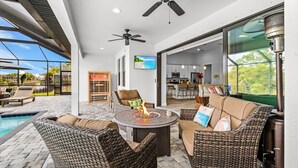 A patio area with wicker furniture, a fire pit, ceiling fans, and a view of the pool and kitchen. - Waterfront Dream! Saltwater Pool, Sauna, & Boat dock 4 bed 3 bath on the water (Cape Coral)