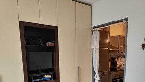 A bedroom with a bed, a wardrobe, a television, and a kitchen visible through an open door. - Farmhouse Tenuta Blueberry - Mirtillo - near airport & Lake Maggiore (Cascinetta)