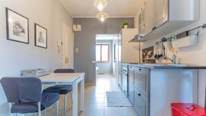 A modern kitchen with a dining area, featuring a white table, grey chairs, and a red trash bin. - Farmhouse Tenuta Blueberry - Mirtillo - near airport & Lake Maggiore (Cascinetta)