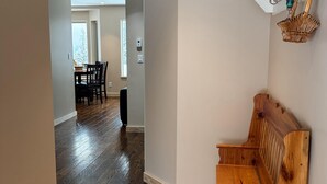 Un hall d’entrée spacieux avec un banc en bois, un coin repas à l’arrière-plan et une étagère blanche avec des paniers.