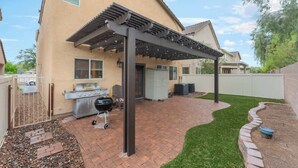 En baghave med grill, pergola og en flisebelagt terrasse.