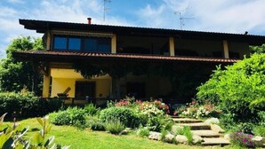 Un bâtiment à deux étages doté d’un balcon, entouré d’un jardin bien entretenu où poussent diverses plantes et fleurs.