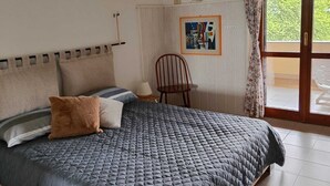 Une chambre à coucher comprenant un lit, une chaise, un luminaire suspendu, un tableau et une porte-fenêtre coulissante donnant sur l’extérieur.