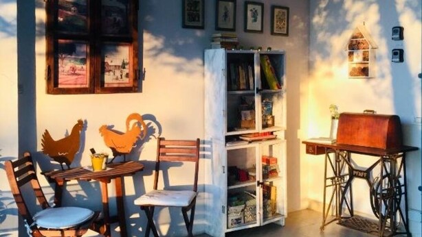 Une pièce avec une table et des chaises en bois, une bibliothèque, une machine à coudre et une fenêtre donnant sur un paysage.