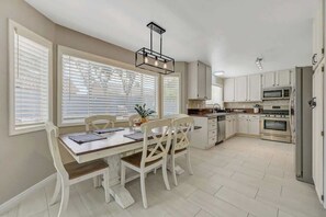 A modern kitchen with white cabinetry, a dining area with a wooden table and white chairs, and a built-in oven. - Prime and Relax Abode (Henderson)