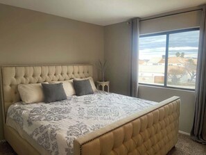 Ein Schlafzimmer mit einem großen Bett, einer gesteppten Kopfteil und Blick nach draußen durch ein Fenster.