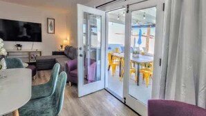 Uma sala de estar moderna com um sofá, cadeiras, uma TV e uma porta de vidro deslizante que dá para uma área de refeições ao ar livre.