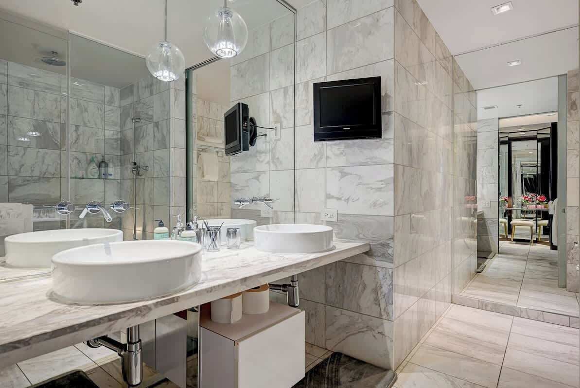 Une salle de bain moderne avec deux lavabos, un grand miroir et un téléviseur fixé au mur.
