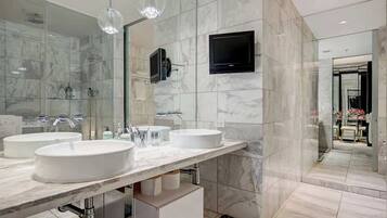 Une salle de bain moderne avec deux lavabos, un grand miroir et un téléviseur fixé au mur.