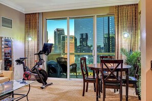 A modern living room with a large sliding glass door leading to a balcony, a stationary exercise bike, a dining table with chairs, and a potted plant. - Fitness Retreat: Private Infrared Sauna w/ Sphere View (Las Vegas)