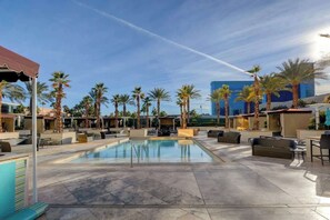 A pool area with lounge seating, palm trees, and a modern building in the background. - Signature Strip View Suite (Las Vegas)