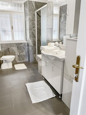 Un baño moderno con piso de mármol, un lavamanos blanco y un espejo grande.