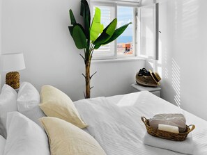 Habitación de hotel con cama, almohadas, lámpara, planta, ventana con vistas y una cesta con toallas.