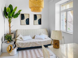 Un dormitorio moderno con cama, una mesa de comedor, una lámpara, una planta y dos cuadros abstractos en la pared.