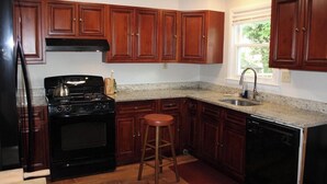 A kitchen with wooden cabinets, a black stove, a sink, and a dishwasher. - Inviting Lanham Suite - Quiet and Close to DC! (Lanham)