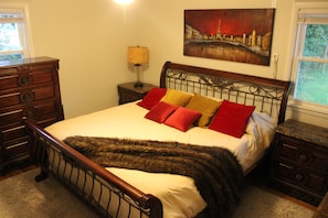 A bedroom with a bed, wooden dresser, nightstand, lamp, and a painting on the wall.