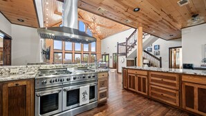 A spacious kitchen with a large island, stainless steel appliances, wooden cabinets, and a high ceiling with exposed beams.