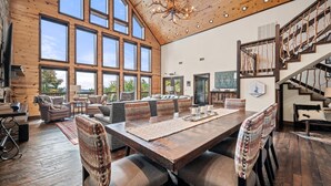A spacious living area with a large wooden dining table, comfortable seating, and a view of the outdoors through large windows.