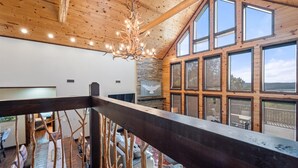A spacious room with a high ceiling, wooden beams, and large windows offering a view of the outdoors.