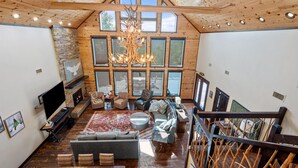 A spacious living room with a fireplace, large windows, and a chandelier.