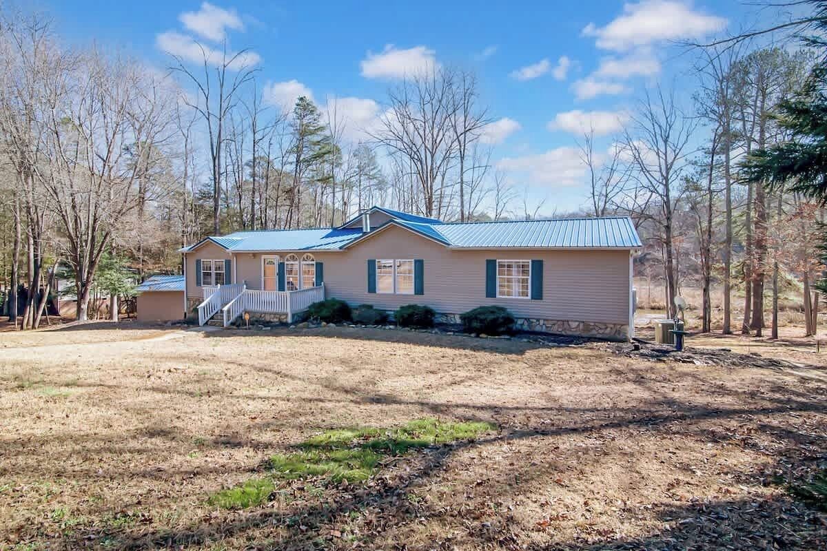 A single-story house with a blue roof, a front porch, and a yard with sparse grass and trees.