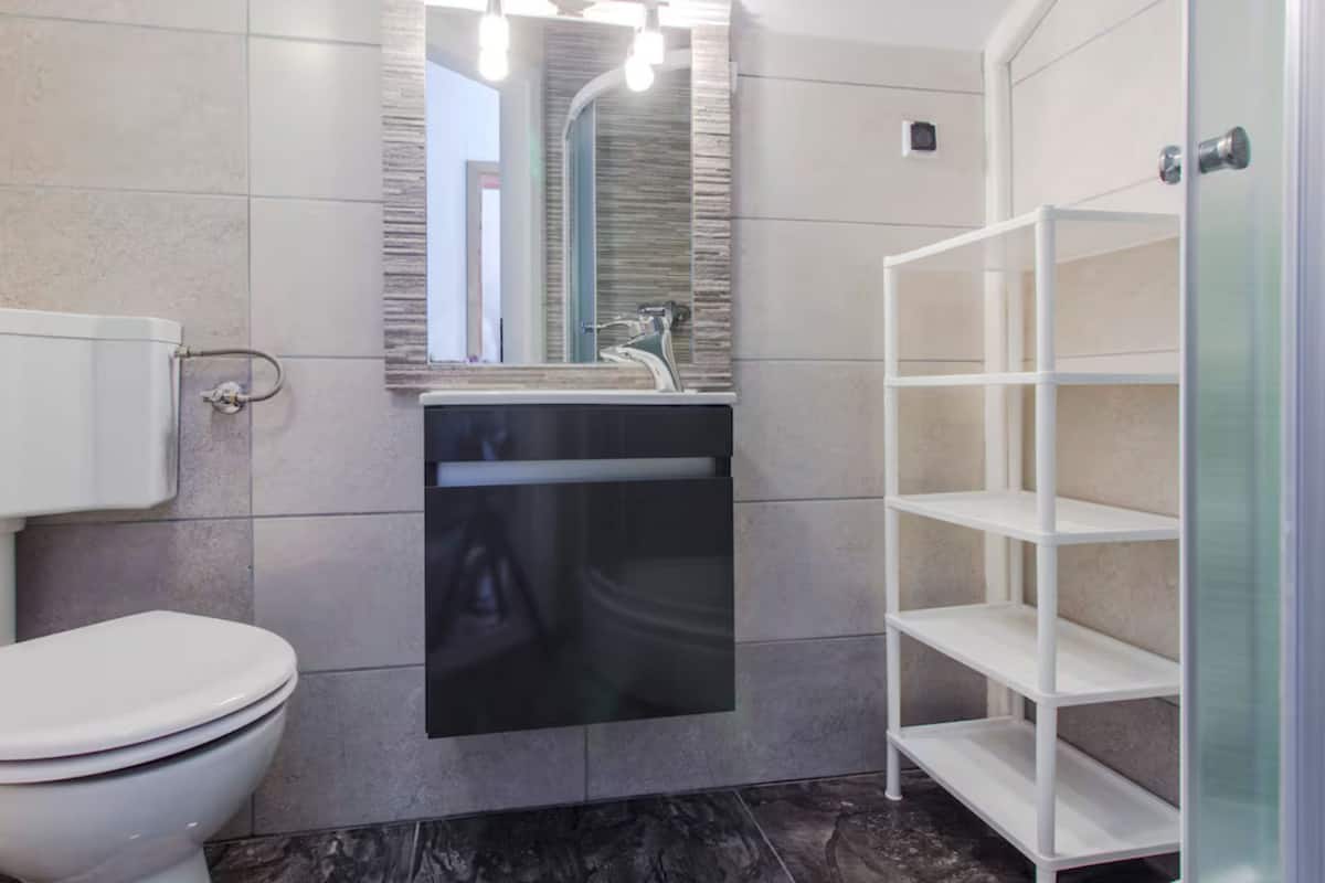 Une salle de bain équipée de toilettes, d’un lavabo, d’un miroir et d’une étagère.