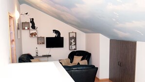 Una sala de estar moderna con techo inclinado, un televisor de pantalla plana, un sofá de cuero negro y un armario de madera.