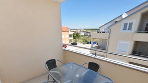 Un balcón con una mesa de vidrio y cuatro sillas, con vista a una zona residencial con edificios y coches aparcados.