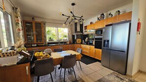 A modern kitchen with wooden cabinets, a stainless steel refrigerator, and a dining area with a table and chairs. - Great vacation home in Madeira, ocean view, in Ponta-do-Sol, heated pool (Ponta do Sol)