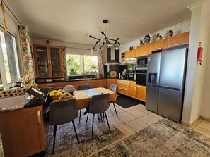 A modern kitchen with wooden cabinets, a stainless steel refrigerator, and a dining area with a table and chairs. - Great vacation home in Madeira, ocean view, in Ponta-do-Sol, heated pool (Ponta do Sol)
