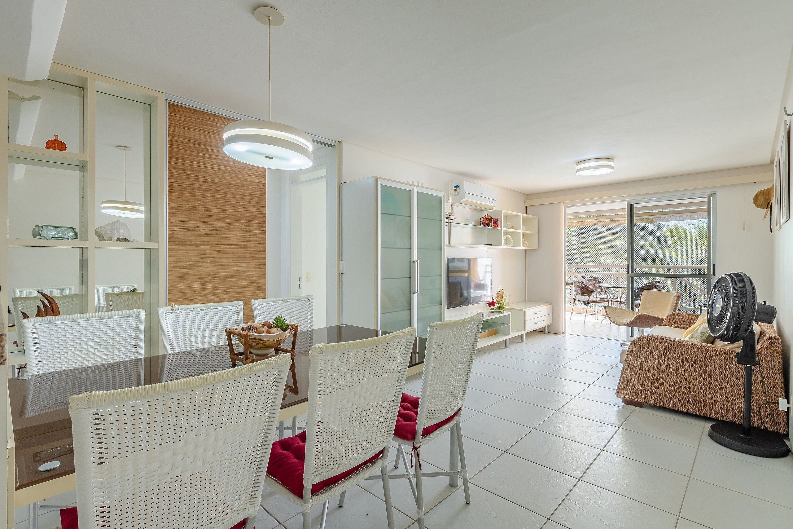 Una sala de estar moderna con comedor, muebles de mimbre blanco y un ventanal grande.