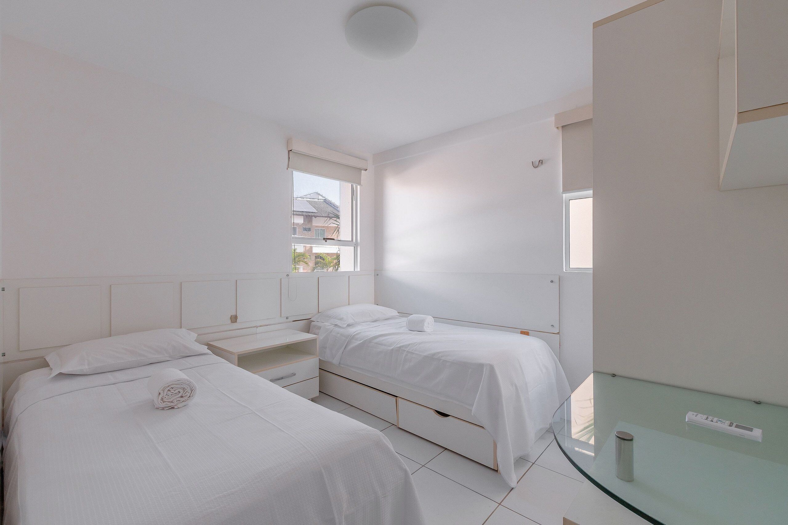 A minimalist bedroom with two beds, a glass table, and a window.