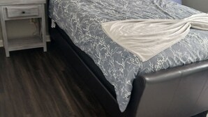 Ein modernes Schlafzimmer mit dunklem Holzboden, einem Bett mit grauem Stoffkopfteil und einem Nachttisch mit Lampe.