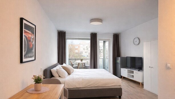 Une chambre d’hôtel moderne équipée d’un lit, d’un bureau, d’une chaise, d’une télévision et d’une horloge murale.
