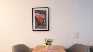 Un coin repas avec une table en bois, deux chaises grises, une petite plante en pot et un tableau encadré au mur.
