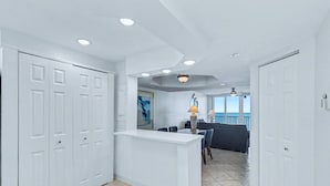 A modern interior with a white reception desk, a dining area with chairs and a table, and a view to an outdoor balcony. - Waterfront Resort Gulf View | Pool & Beach Access (Clearwater)