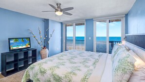 A bedroom with a bed, a TV, a ceiling fan, and a view of the ocean through a sliding door. - Waterfront Resort Gulf View | Pool & Beach Access (Clearwater)