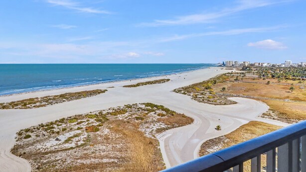 A coastal view with a sandy beach, a winding road, and a cityscape in the background. - Waterfront Resort Gulf View | Pool & Beach Access (Clearwater)
