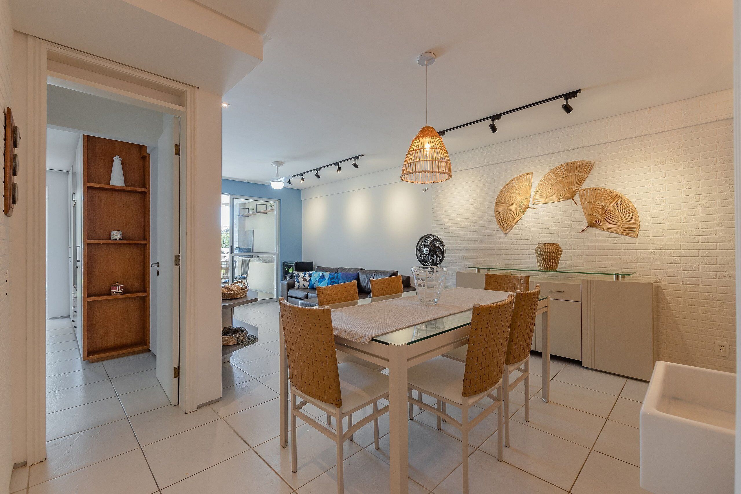 Un comedor moderno con una mesa de vidrio, sillas de mimbre y una lámpara colgante.