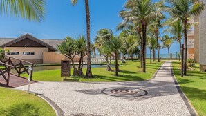 A paved pathway with a circular design, surrounded by palm trees and a building with a tiled roof. - Portamaris Resort - Luxury Apartment by Carpediem (Aquiraz)