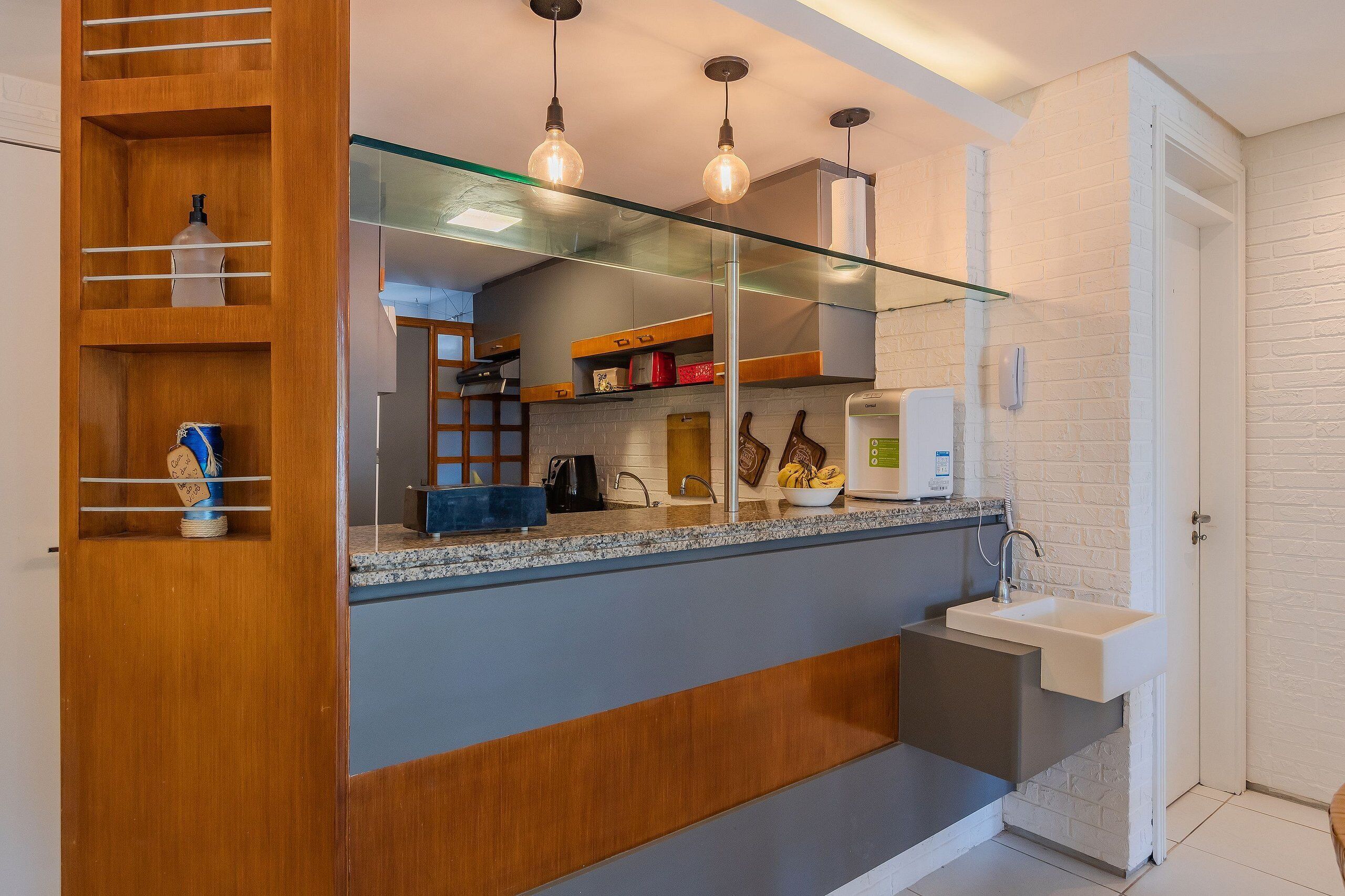 Una cocina moderna con separador de vidrio, repisas de madera y un lavamanos empotrado.