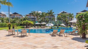 A pool area with lounge chairs and umbrellas, surrounded by palm trees and a clear blue sky. - Portamaris Resort - Luxury Apartment by Carpediem (Aquiraz)