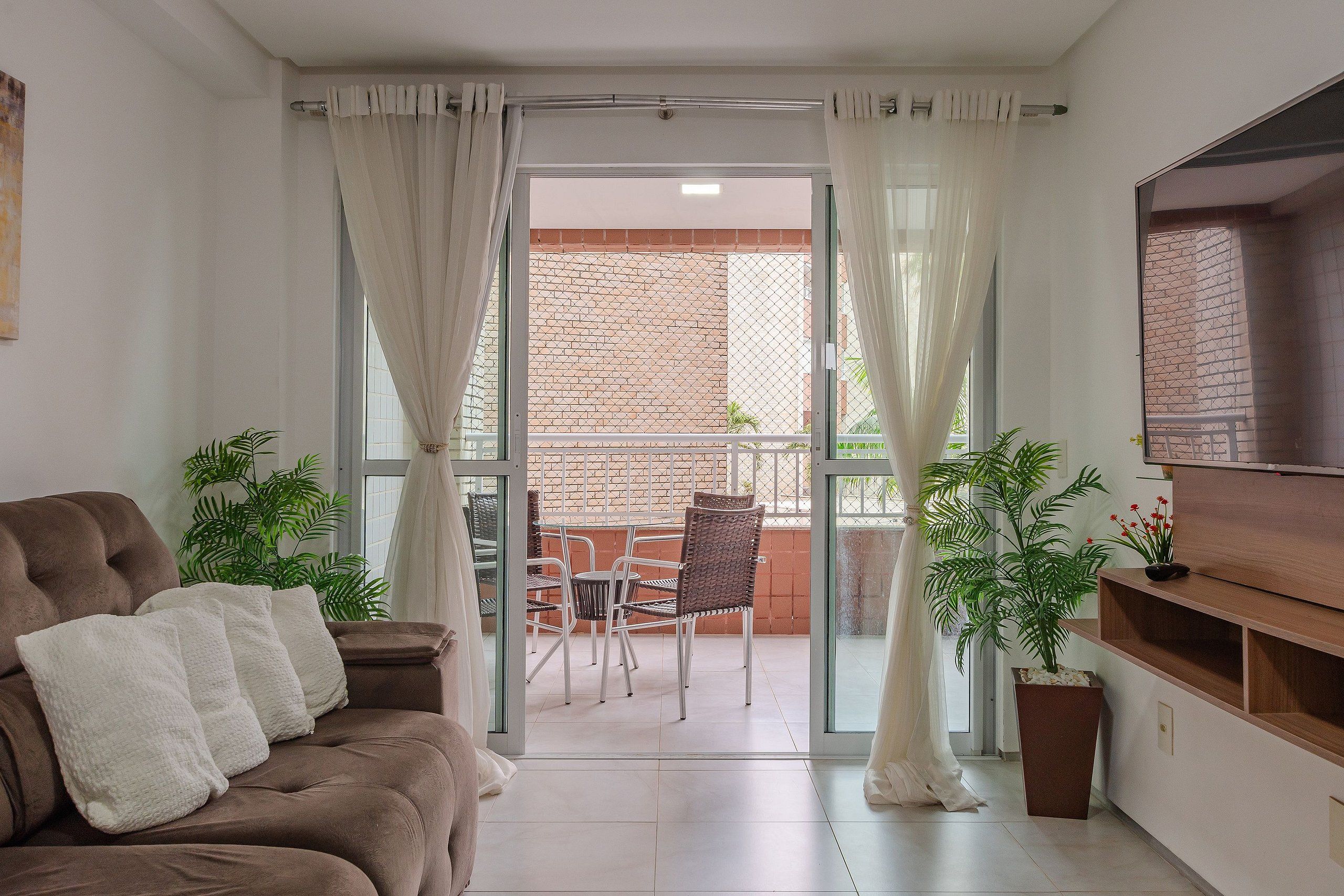Una sala de estar con sofá, televisor y puerta corrediza de vidrio que da a un balcón con mesa y sillas.